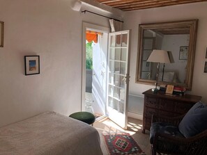 Une chambre à coucher comprenant un lit, une commode, une chaise, un miroir et une porte donnant sur un balcon.