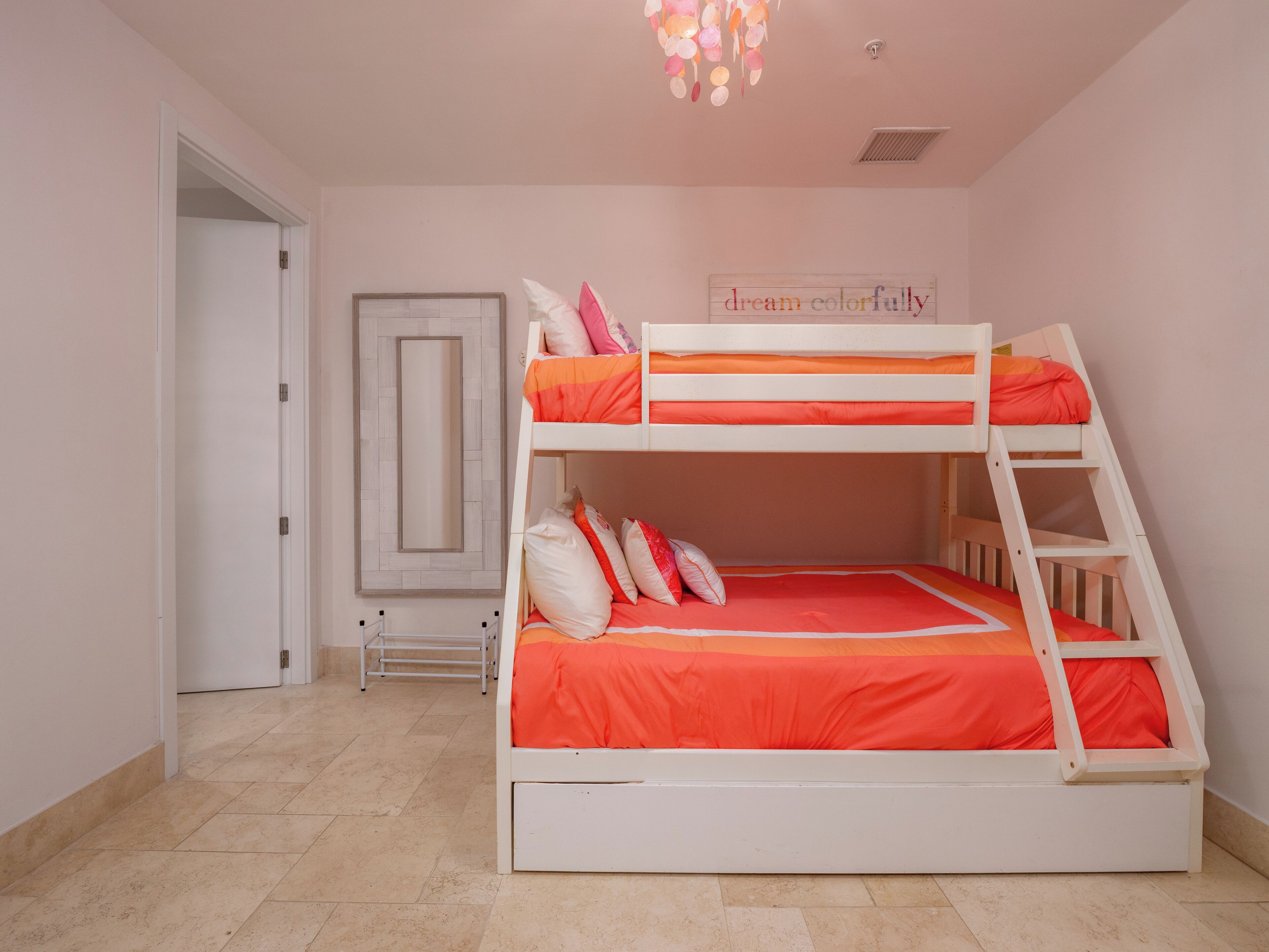 A bunk bed with orange bedding, a ladder, and a wall-mounted shelf.