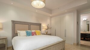 A bedroom with a large bed, a nightstand, a dresser, a wardrobe, and a bathroom visible through an open door. - Charming Beachfront 3BR in Puntarena (Río Hato)