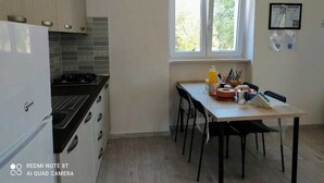 Cocina compacta con estufa a gas, refrigerador y mesa de comedor con sillas. Una ventana ofrece luz natural.