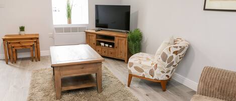A living room with a wooden coffee table, a sofa, a TV stand, and a small table with a plant.