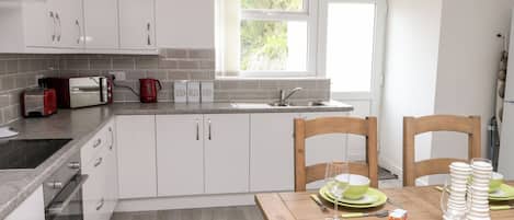 A modern kitchen with white cabinets, a wooden dining table set with green plates, and a window providing natural light.