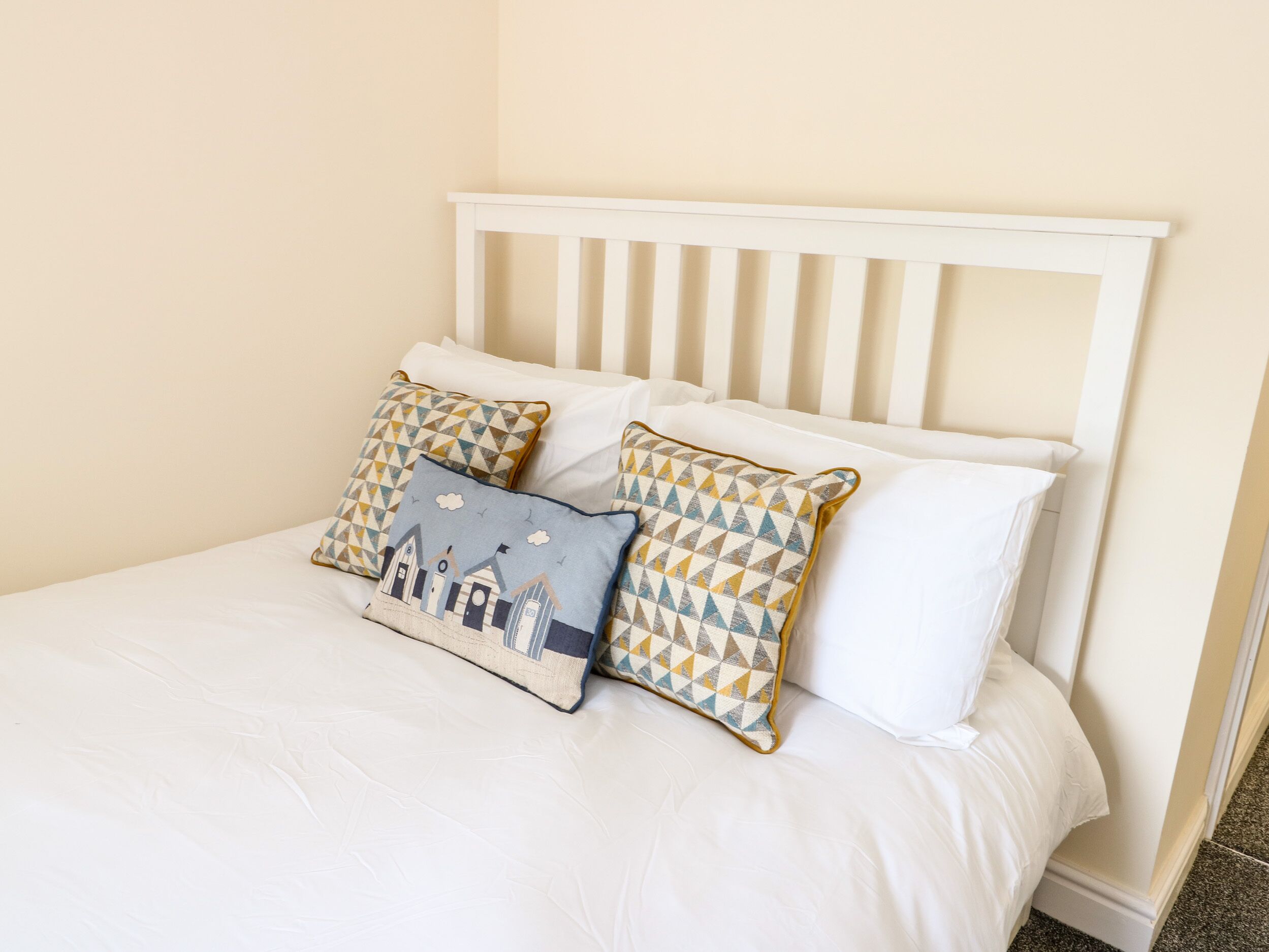 A bed with white bedding and two patterned pillows.