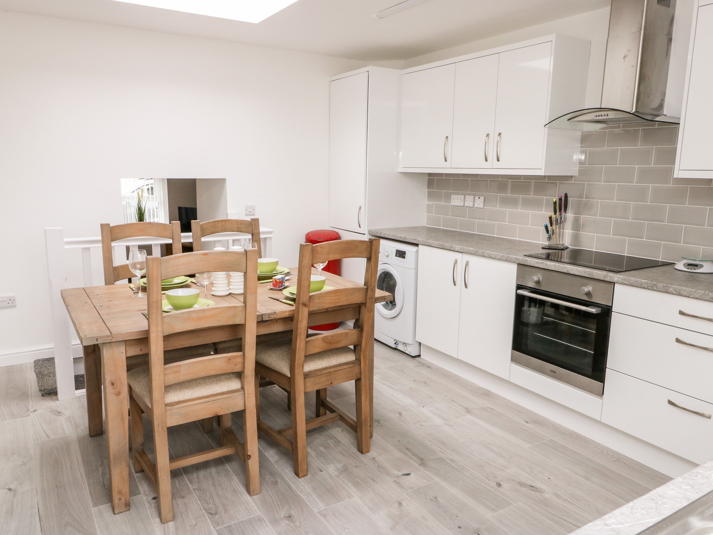 Een moderne keuken met witte kastjes, een ingebouwde oven en een eethoek met houten stoelen en een tafel.