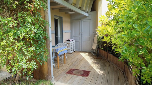 A wooden deck with a table and chairs, a door, and a small garden area.
