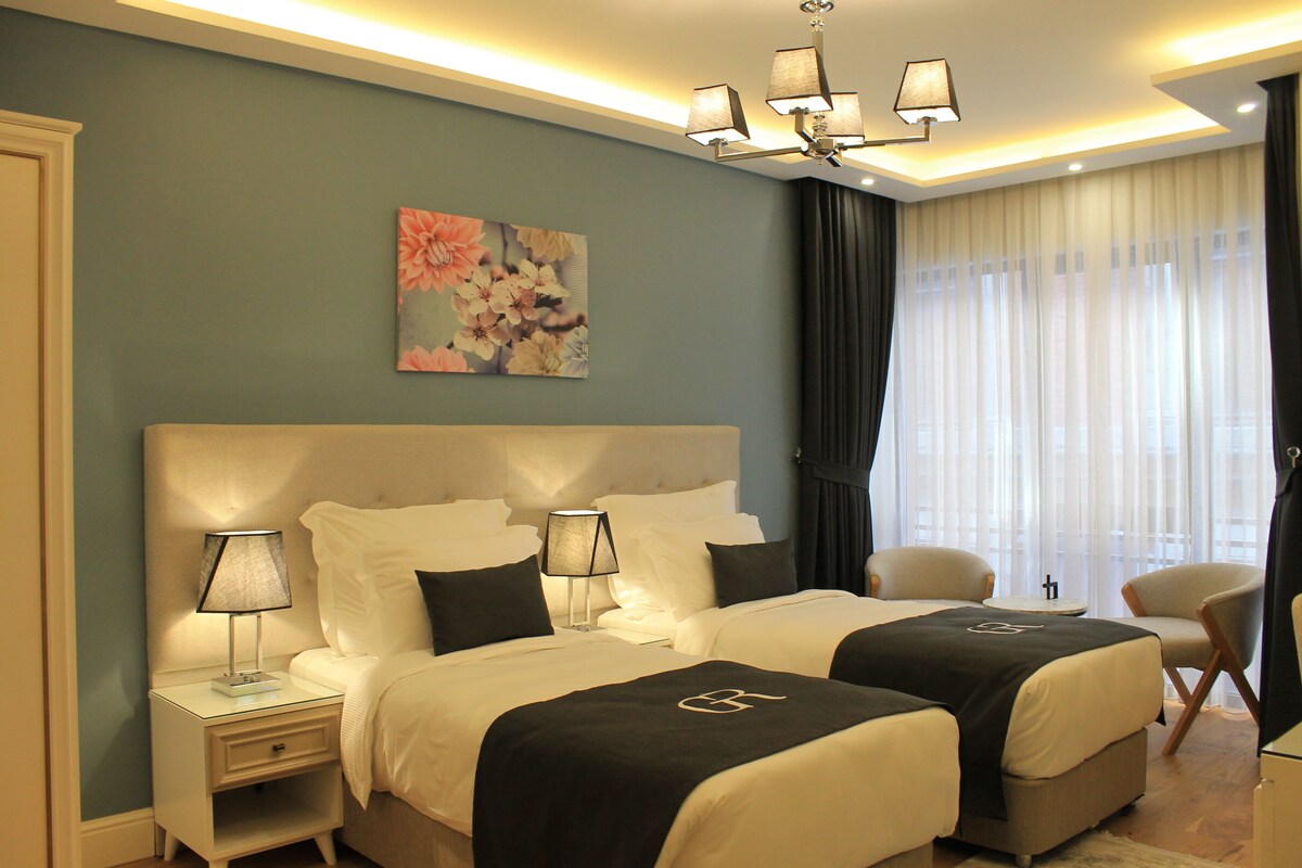 Une chambre d’hôtel avec deux lits, une table de chevet avec une lampe, une chaise et un tableau au mur.