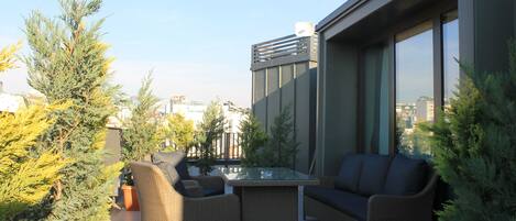 A modern outdoor seating area with wicker furniture and potted plants, overlooking a cityscape.