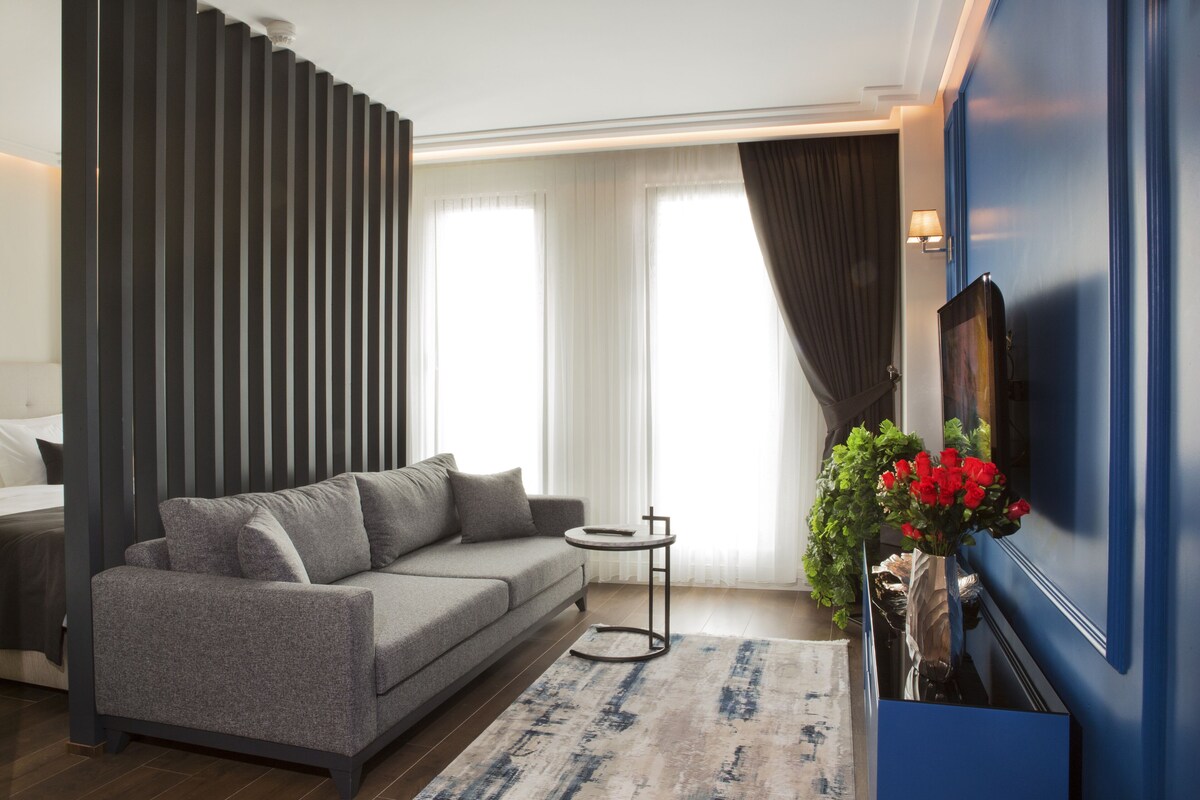 Un salon moderne avec un canapé gris, une petite table d’appoint, un vase rempli de fleurs rouges et un grand téléviseur fixé au mur.
