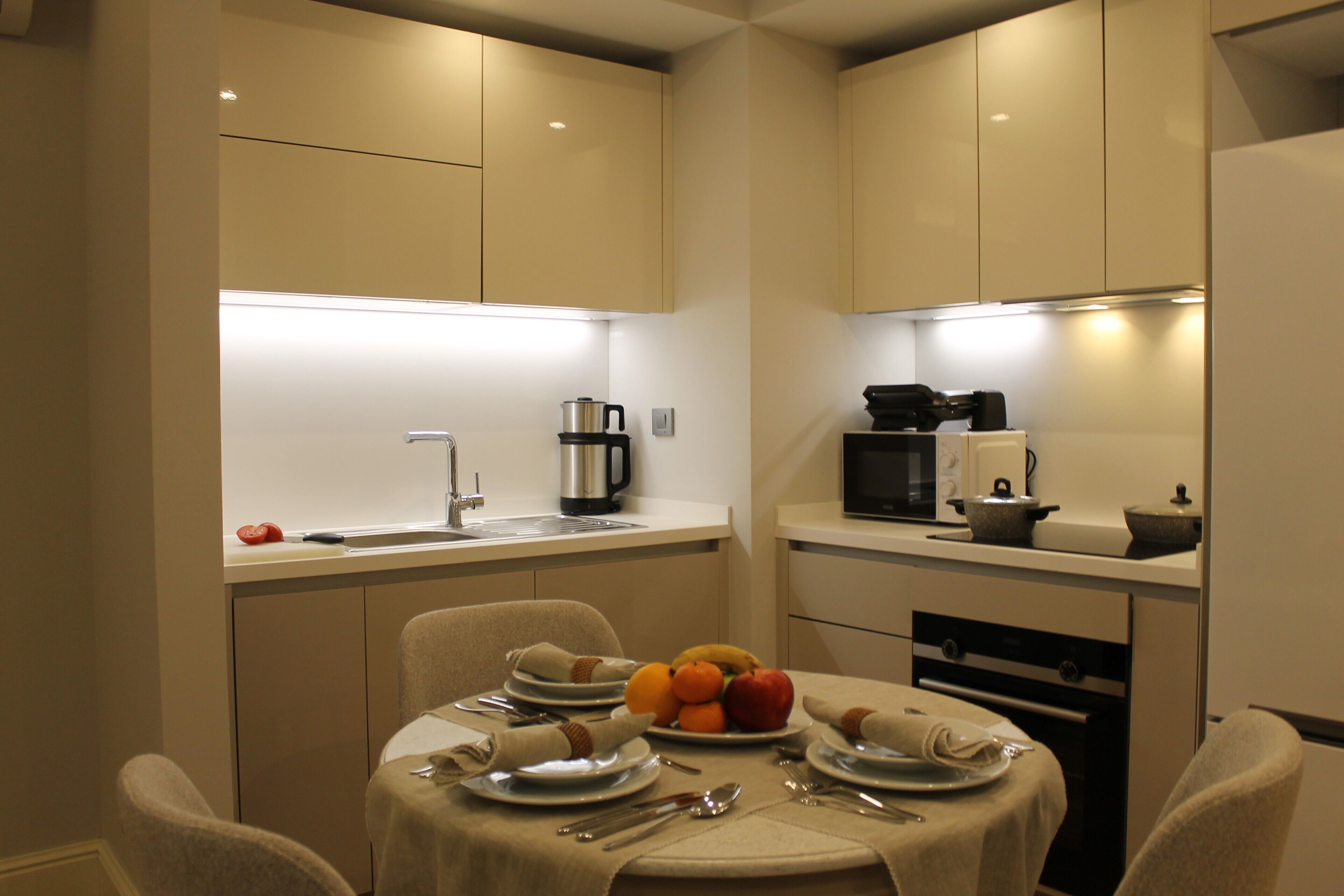 A compact kitchen with modern appliances, a dining table set for two, and a fruit bowl on the table.