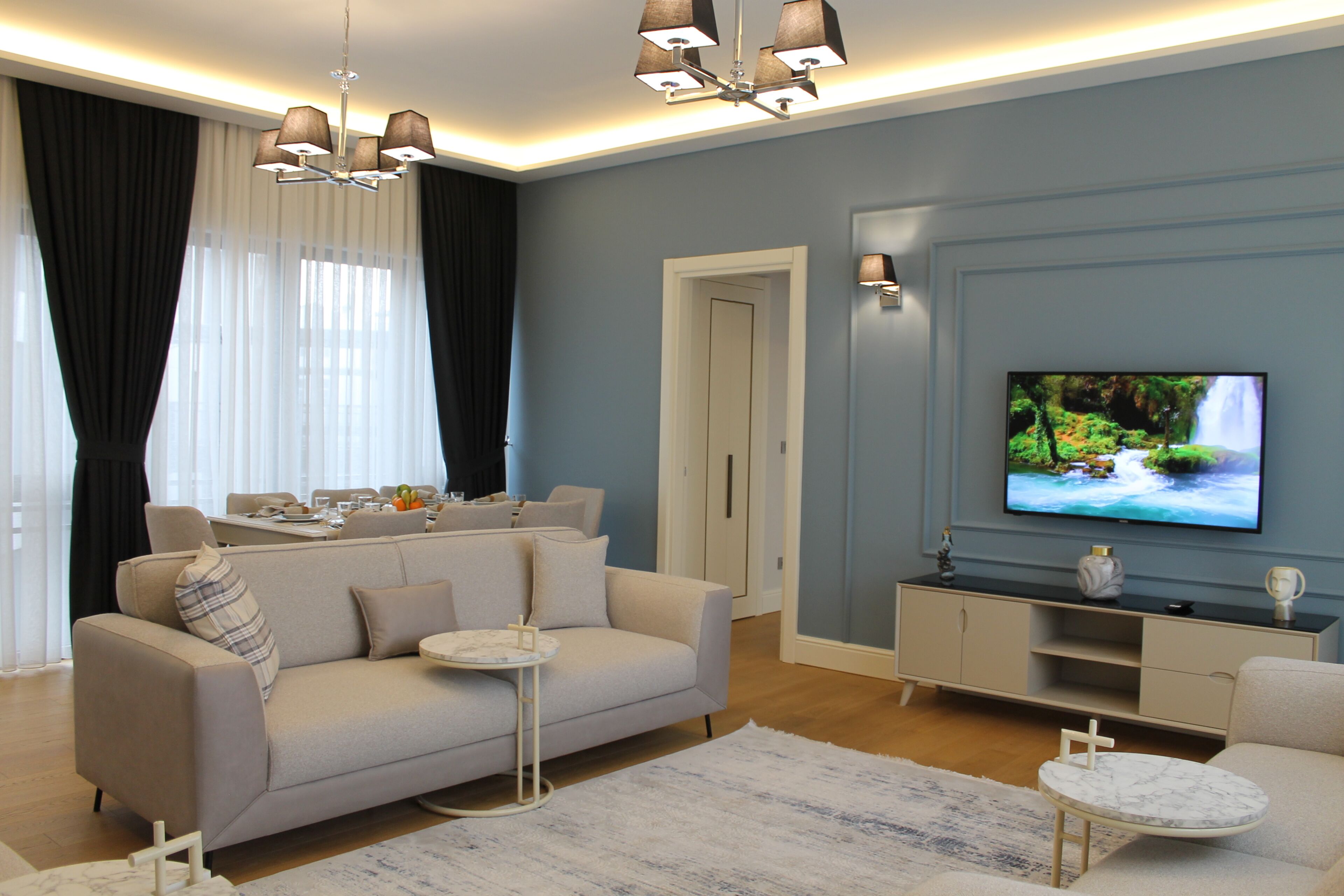 A modern living room with a sofa, coffee table, TV, and a dining area with a table and chairs.