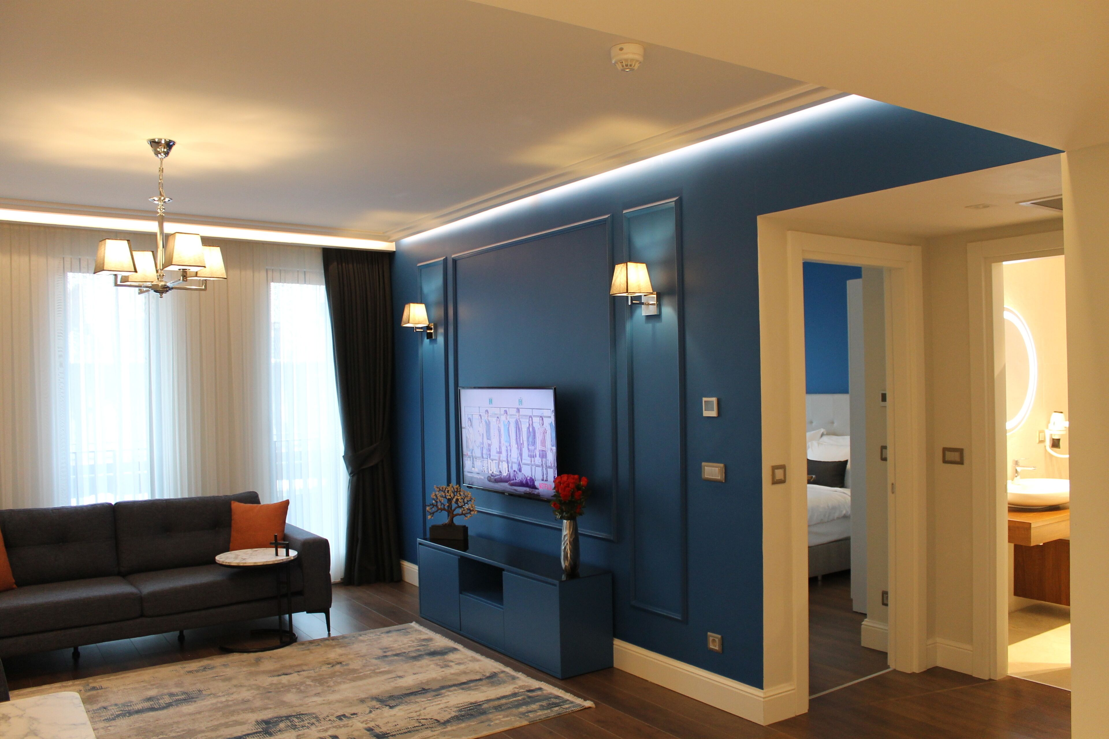Een moderne woonkamer met een donkerblauwe accentmuur, een flatscreen televisie, een bank en een kroonluchter.