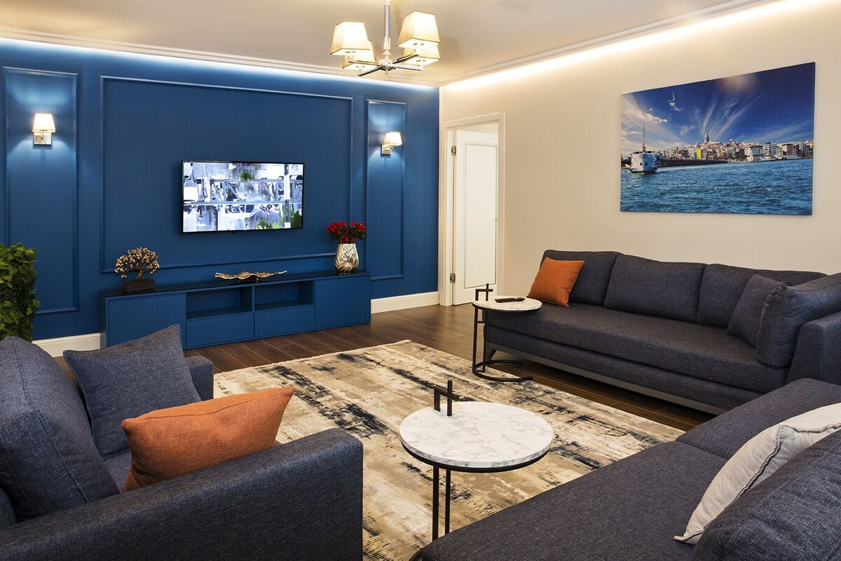 Un salon moderne avec un mur d’accent bleu, un téléviseur à écran plat, un ensemble de canapés et une table basse.