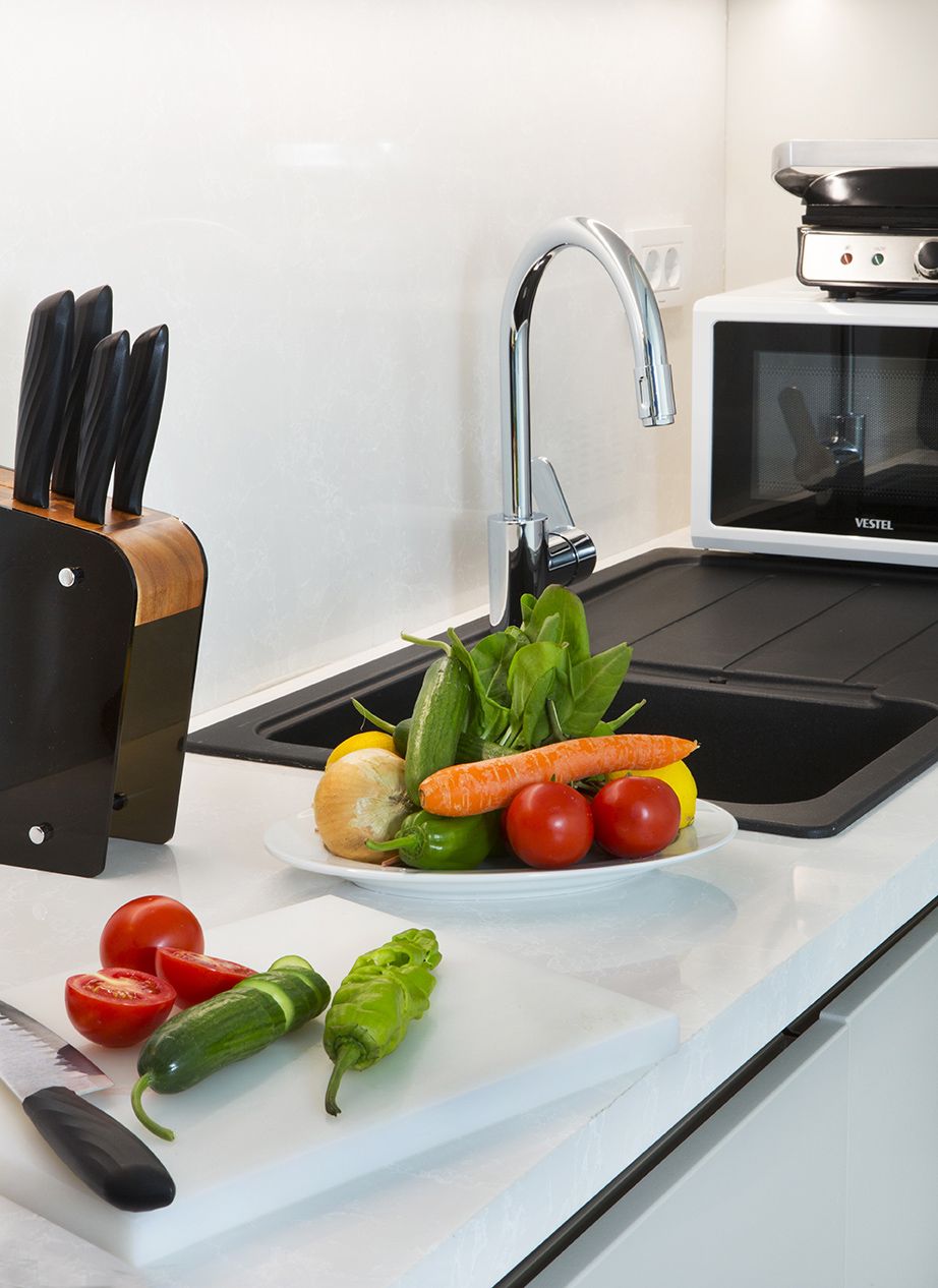 A kitchen with a sink, a microwave, and a cutting board with vegetables.