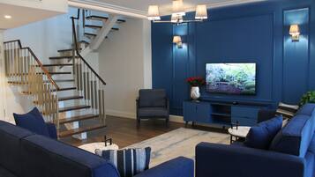 A modern living room with a blue accent wall, a flat-screen TV, a staircase, and a seating area with sofas and a coffee table.