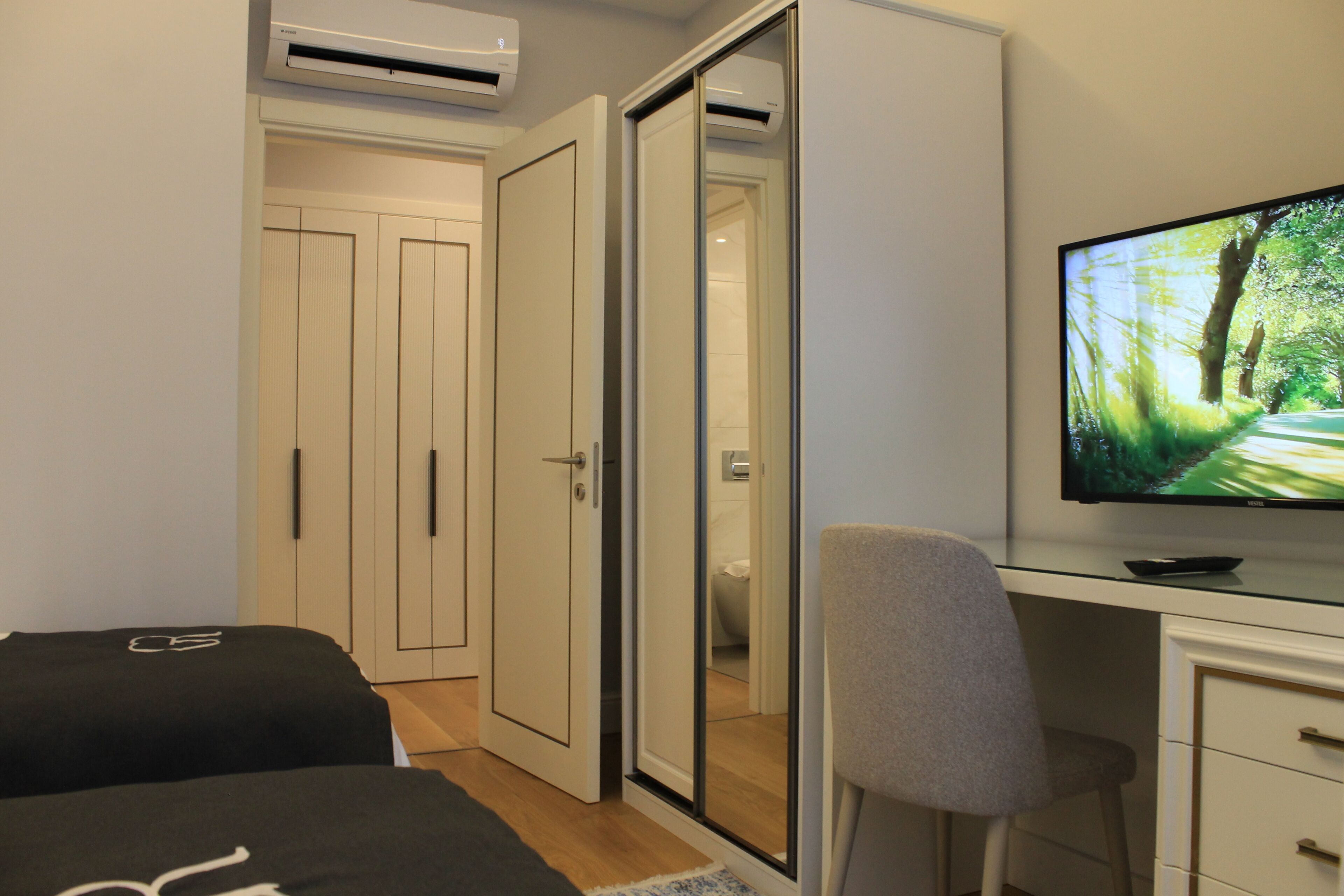 A bedroom with a bed, a desk, a chair, a TV, and a wardrobe.
