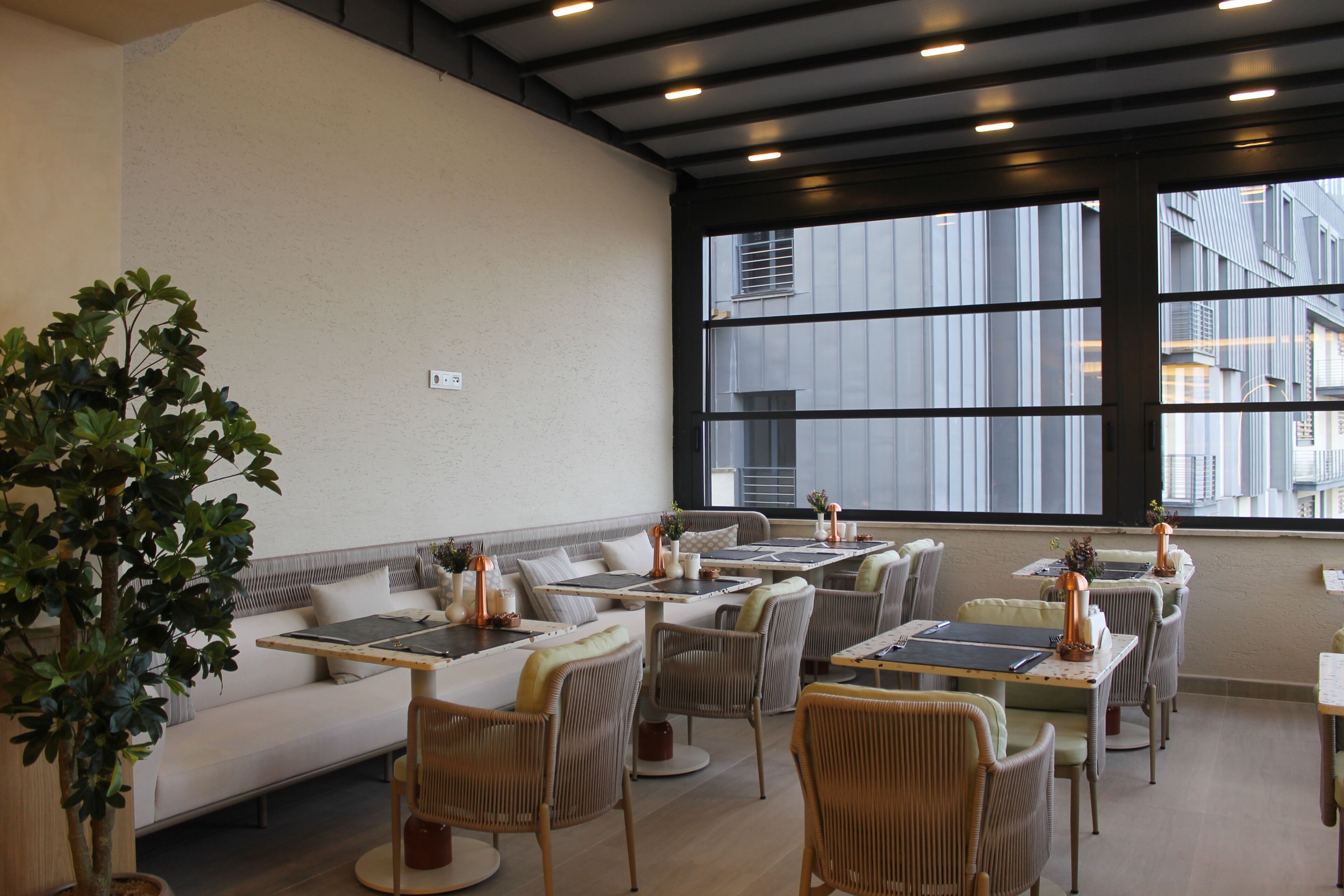 A modern dining area with wicker furniture, a sofa, and large windows offering a view of buildings.