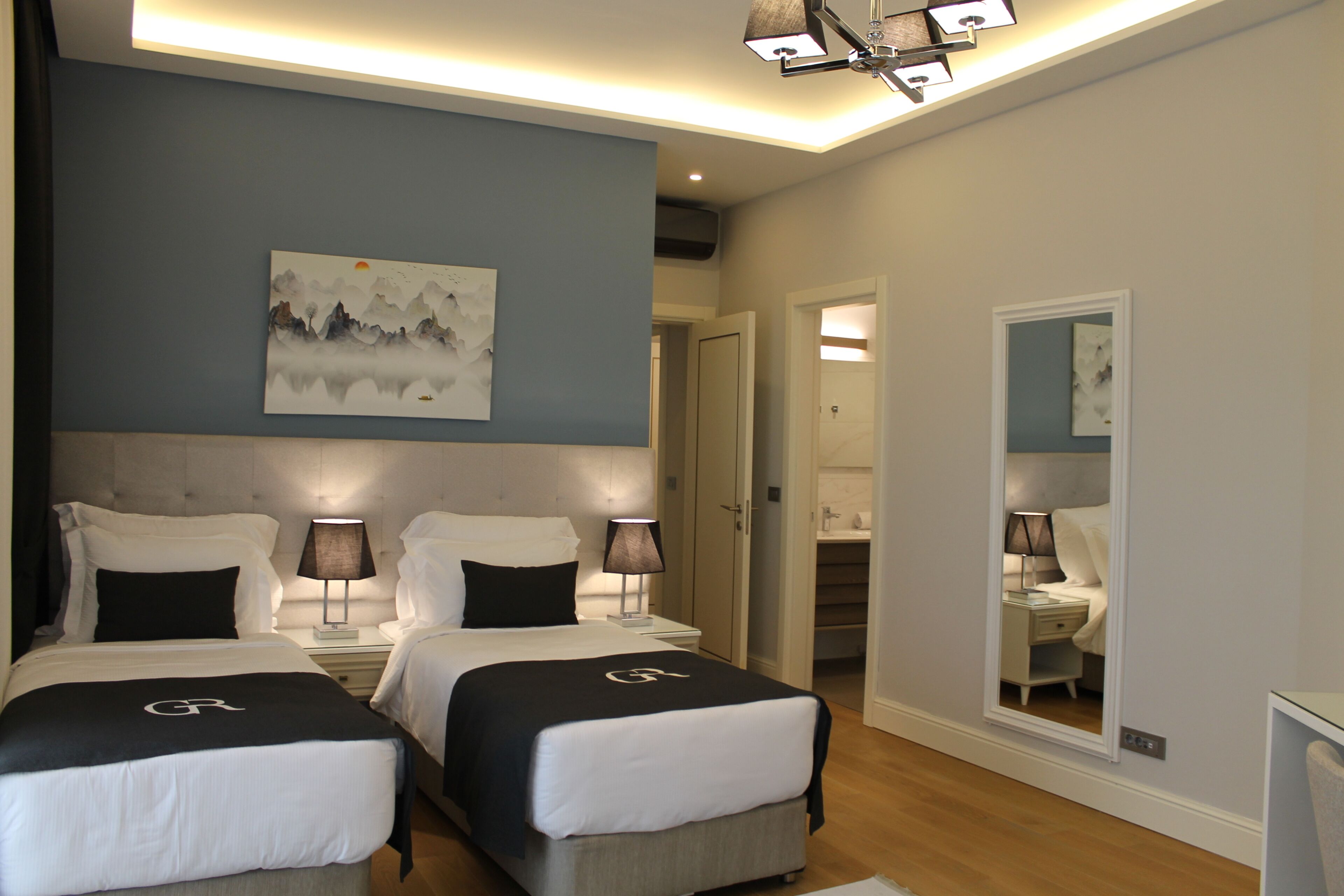 Une chambre d’hôtel avec deux lits, un tableau au mur, un miroir et un luminaire au plafond.