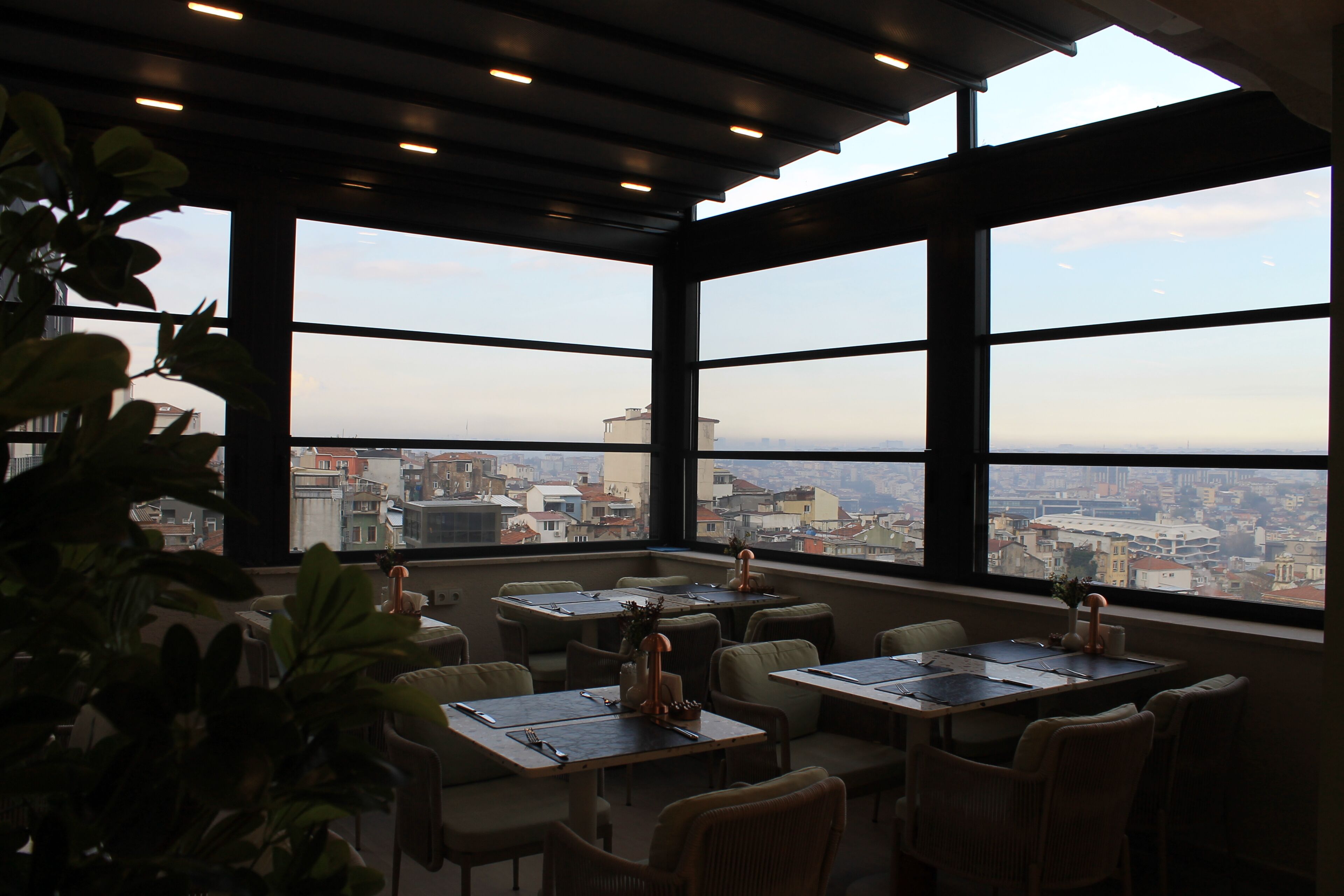 A restaurant with tables and chairs, large windows, and a view of a cityscape.