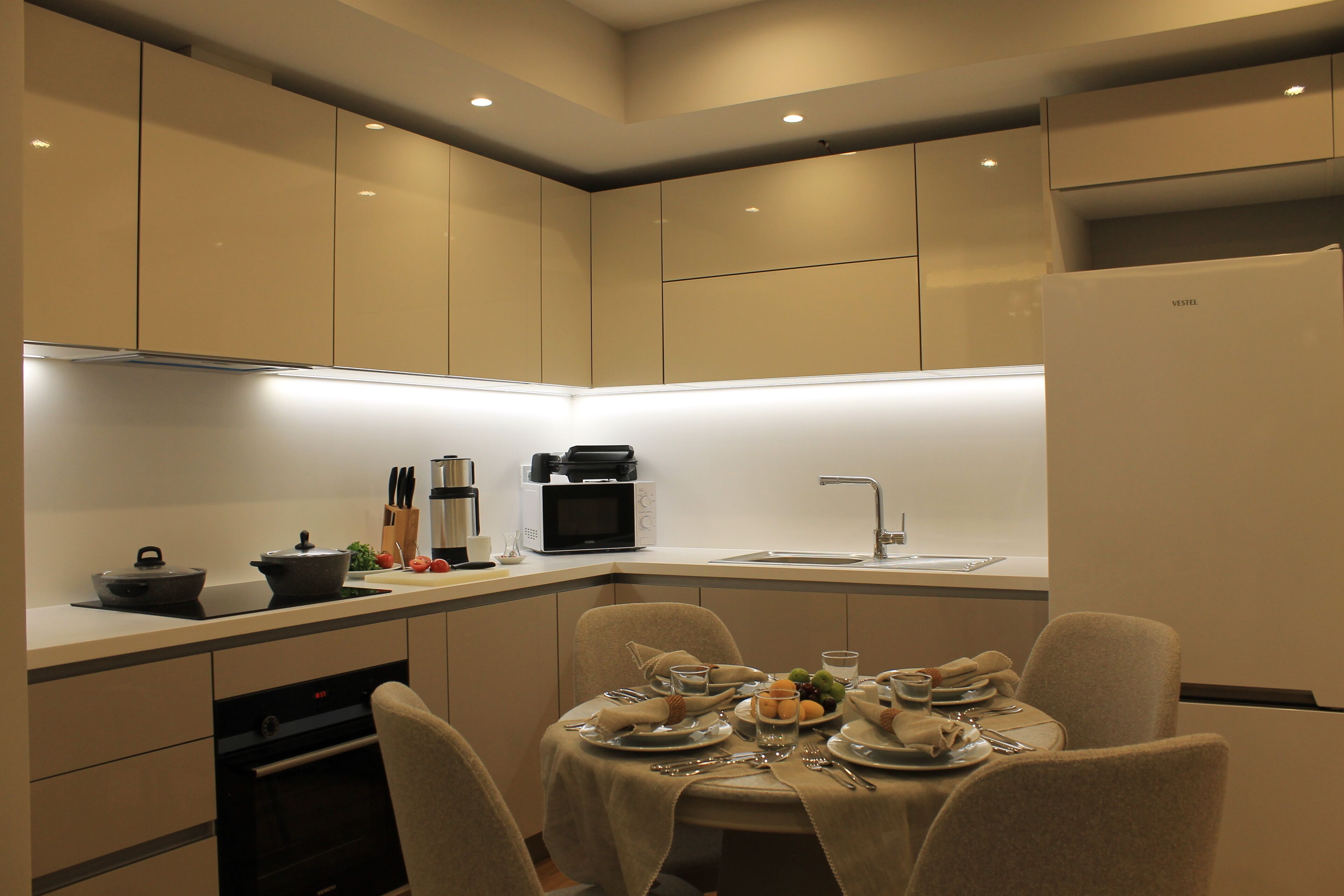 Une cuisine moderne dotée d’appareils électroménagers intégrés, un coin repas avec une table dressée pour quatre personnes et un four compact.