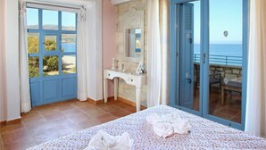 Een slaapkamer met een bed, een kaptafel en uitzicht op zee.