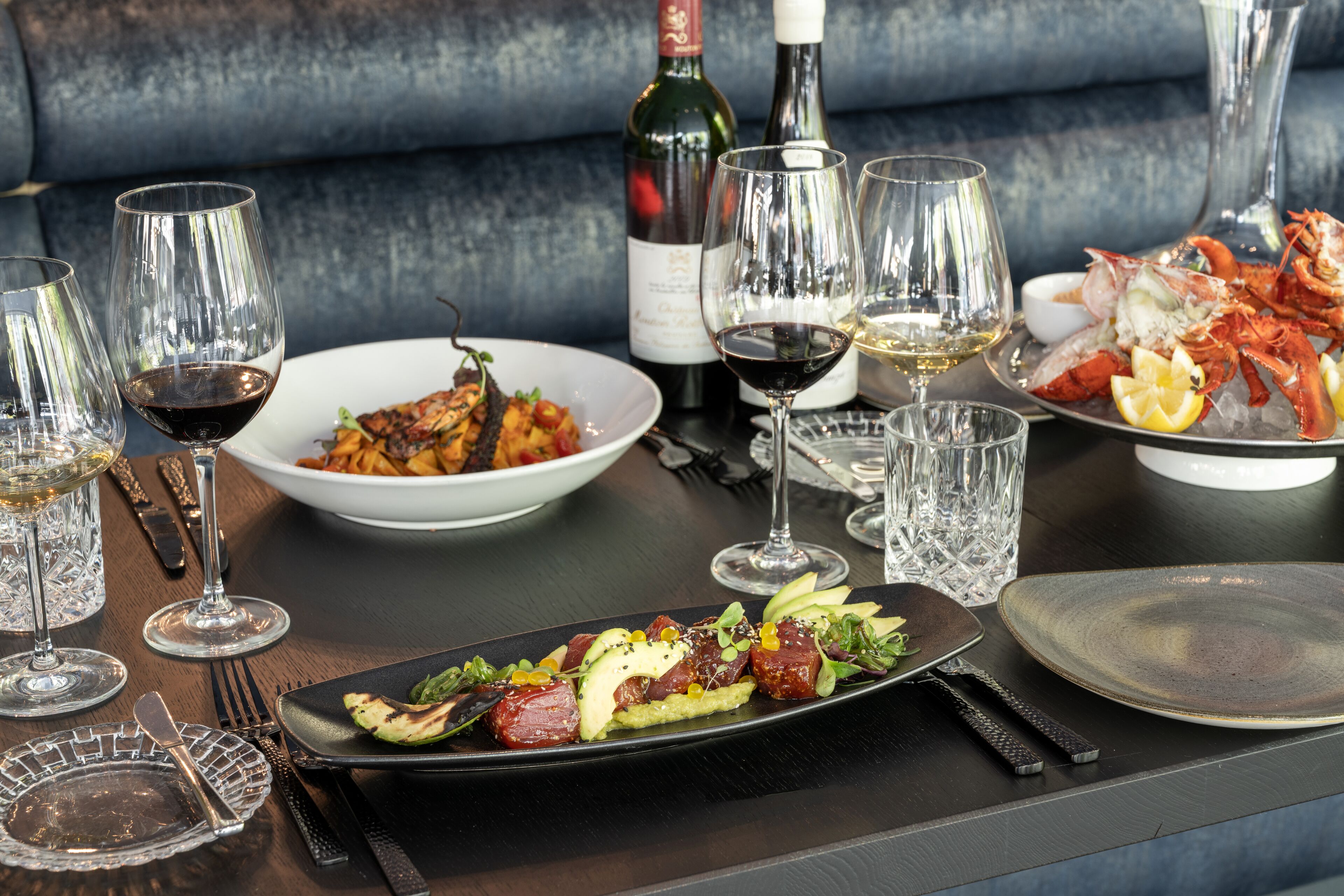 A dining table set with plates of food, wine glasses, and a bottle of wine.