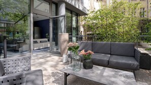 Un área de estar al aire libre con un sofá, sillas y una mesa. Hay jarrones con flores sobre la mesa.