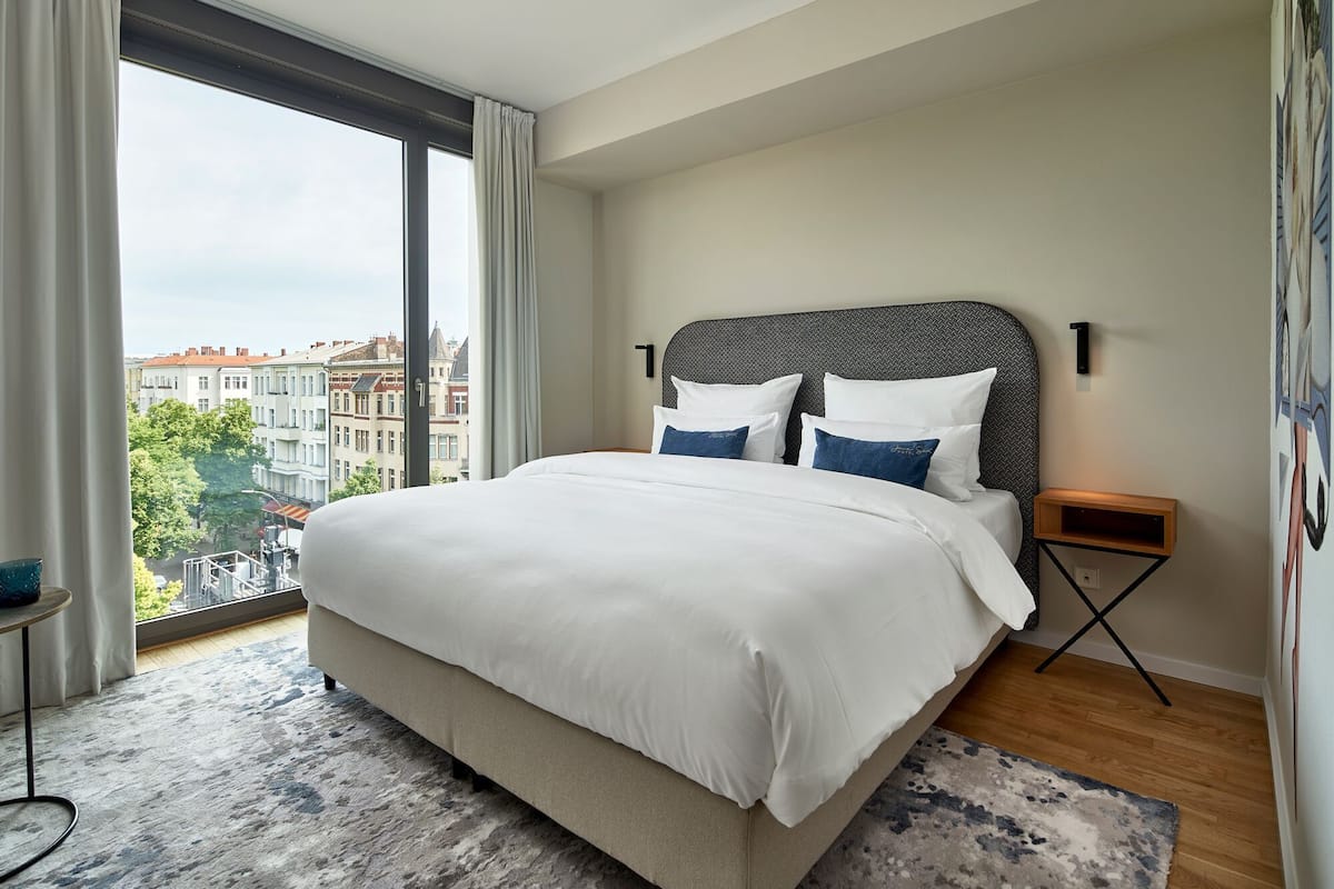 Une chambre d’hôtel moderne avec un grand lit, une vue sur la ville et une petite table de chevet.