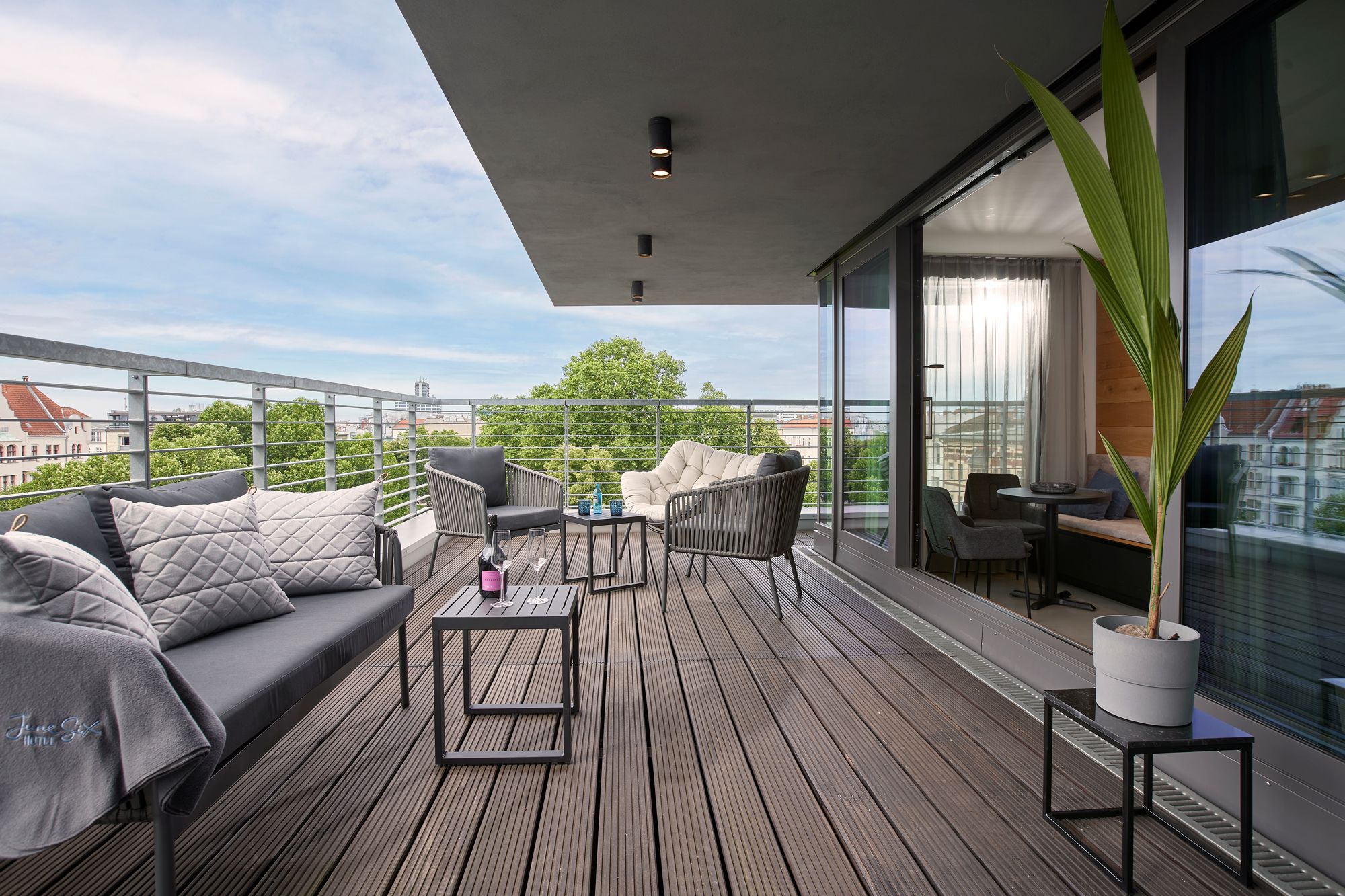 A modern balcony with a sofa, chairs, and a table, overlooking a cityscape.