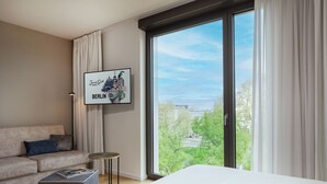 Una habitación de hotel moderna con un ventanal grande, un cuadro enmarcado de Berlín, un sofá y una mesita auxiliar pequeña.