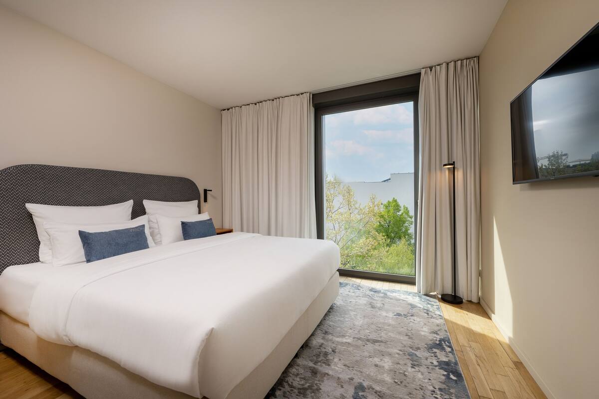 Une chambre moderne avec un grand lit, une vue sur l’extérieur et un téléviseur à écran plat fixé au mur.