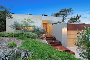 A modern house with a stone facade, a wooden staircase, and a garden with various plants and flowers.