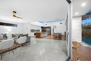 A modern kitchen with a central island, a dining area with a wooden table, and a poolside deck.