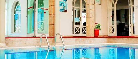 A swimming pool with clear blue water, surrounded by arched windows and doors, and a red trim along the pool edge.