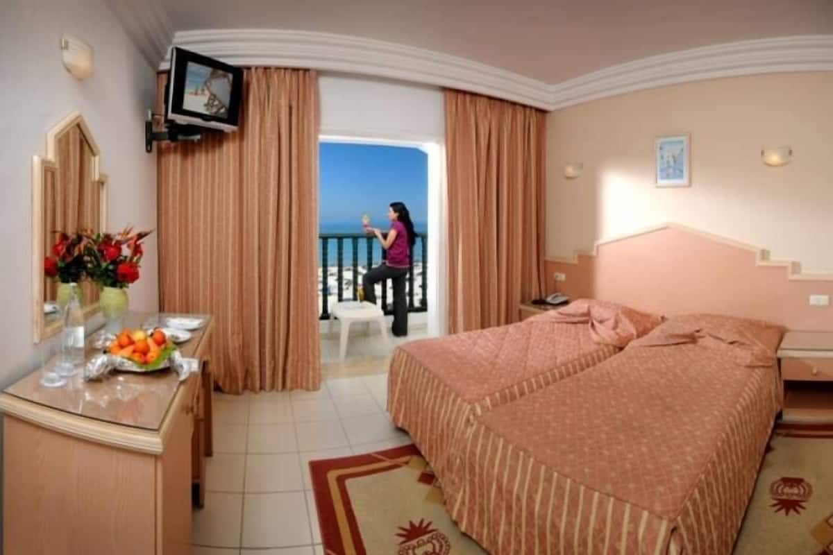 A hotel room with a bed, a desk with a vase of flowers, a television, and a balcony with a view.