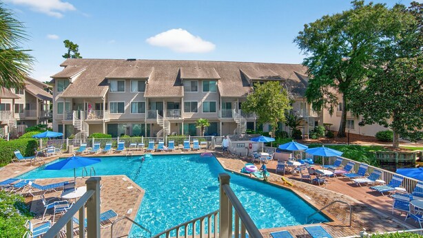 A hotel with a swimming pool, multiple balconies, and outdoor seating areas. - Courtside 60 - 3BR Spacious Townhouse - Pool View - Short Walk to Beach (Hilton Head Island)