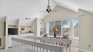 A spacious living room with a high ceiling, a television, a dining area with chairs, and large windows with blinds. - Courtside 60 - 3BR Spacious Townhouse - Pool View - Short Walk to Beach (Hilton Head Island)