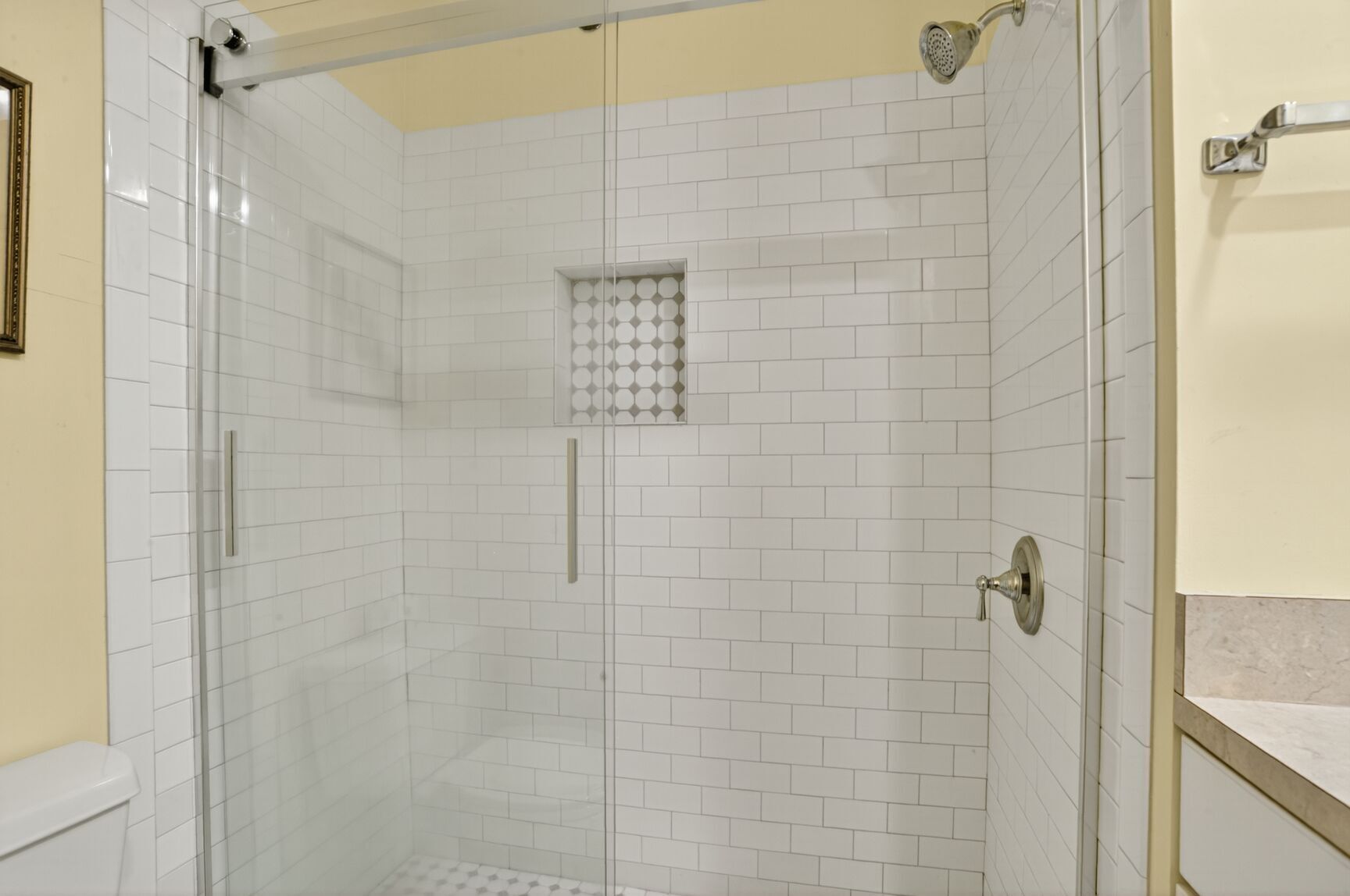 Una ducha con azulejos blancos y puerta de cristal.