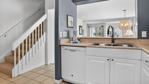 A modern kitchen with a built-in dishwasher, a stainless steel sink, and a large mirror above the countertop. - Courtside 60 - 3BR Spacious Townhouse - Pool View - Short Walk to Beach (Hilton Head Island)