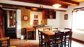 A cozy kitchen with a dining area, featuring wooden beams, a stone wall, and a tiled floor.