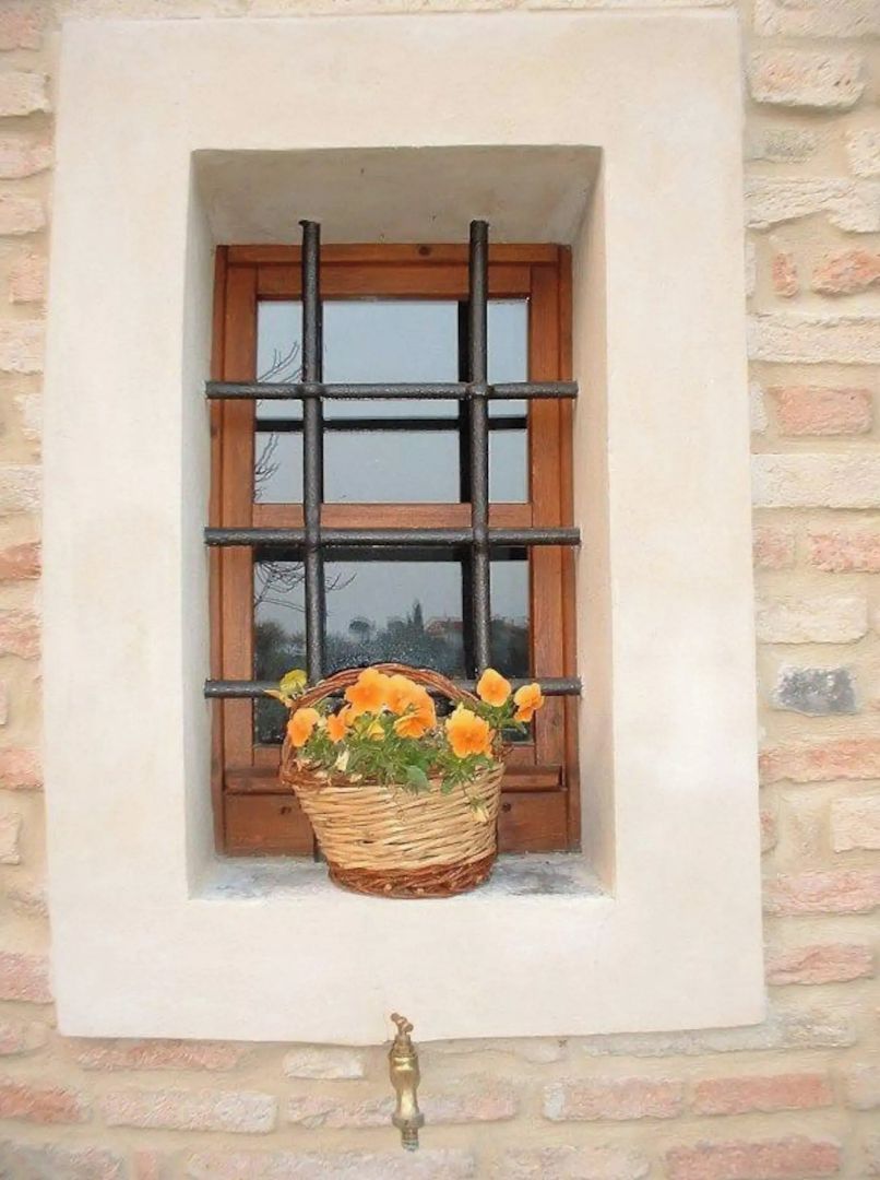 Une fenêtre avec un cadre en bois et une grille en métal, un panier en osier rempli de fleurs et une poignée de porte en laiton.