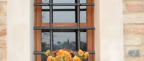 Une fenêtre avec un cadre en bois et une grille en métal, un panier en osier rempli de fleurs et une poignée de porte en laiton.