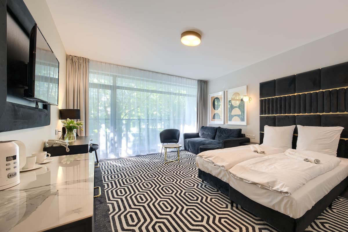 A modern hotel room with a large bed, a sofa, a desk with a telephone, and a TV mounted on the wall.