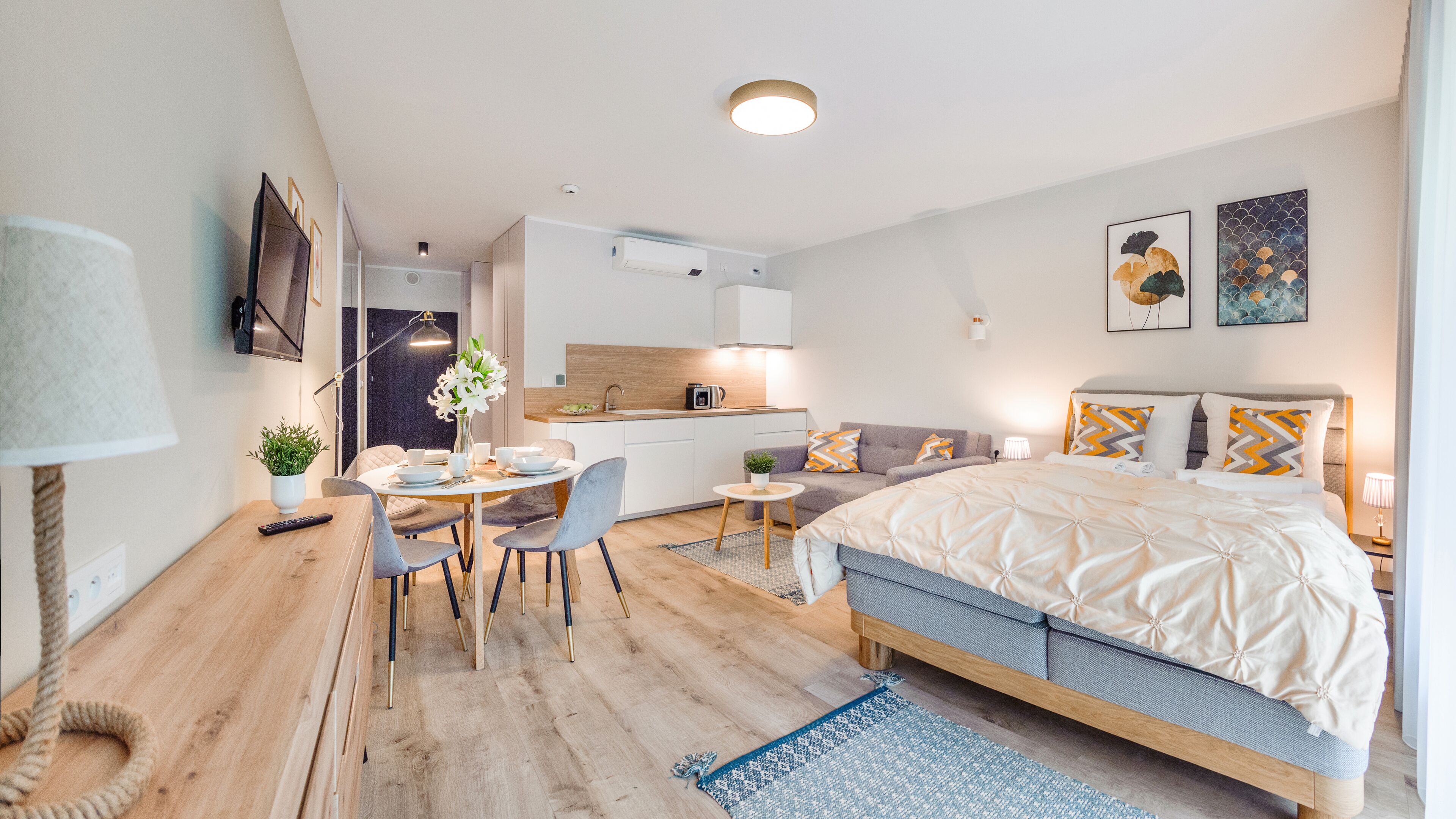 A modern hotel room with a bed, a sofa, a dining area, and a kitchenette.