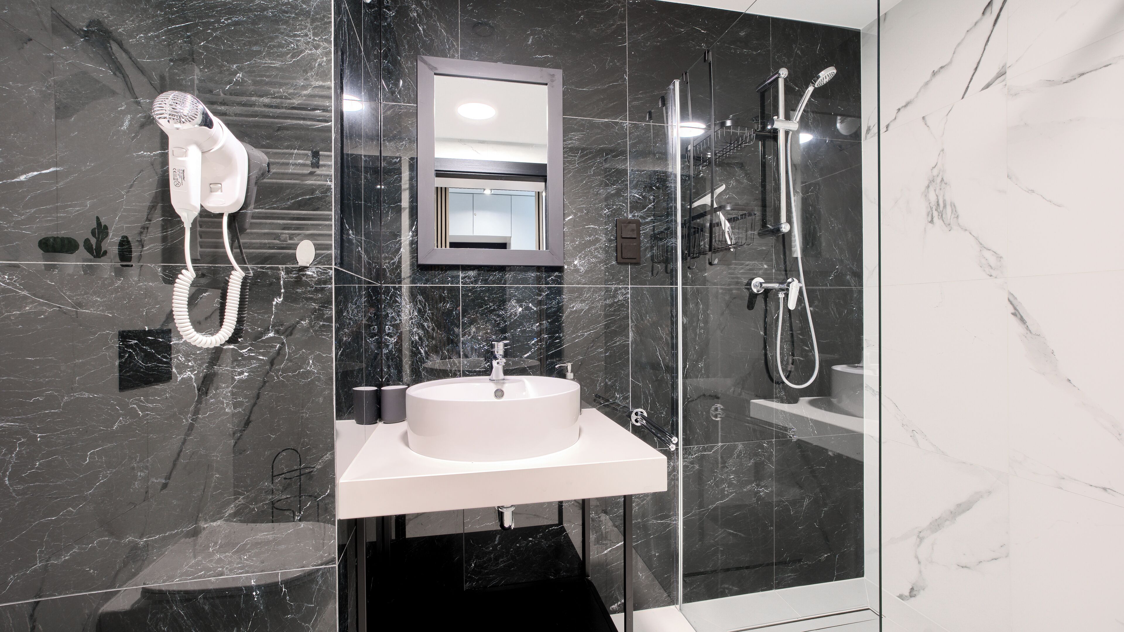 Un baño moderno con ducha de vidrio, secador de pelo integrado y un lavabo blanco.