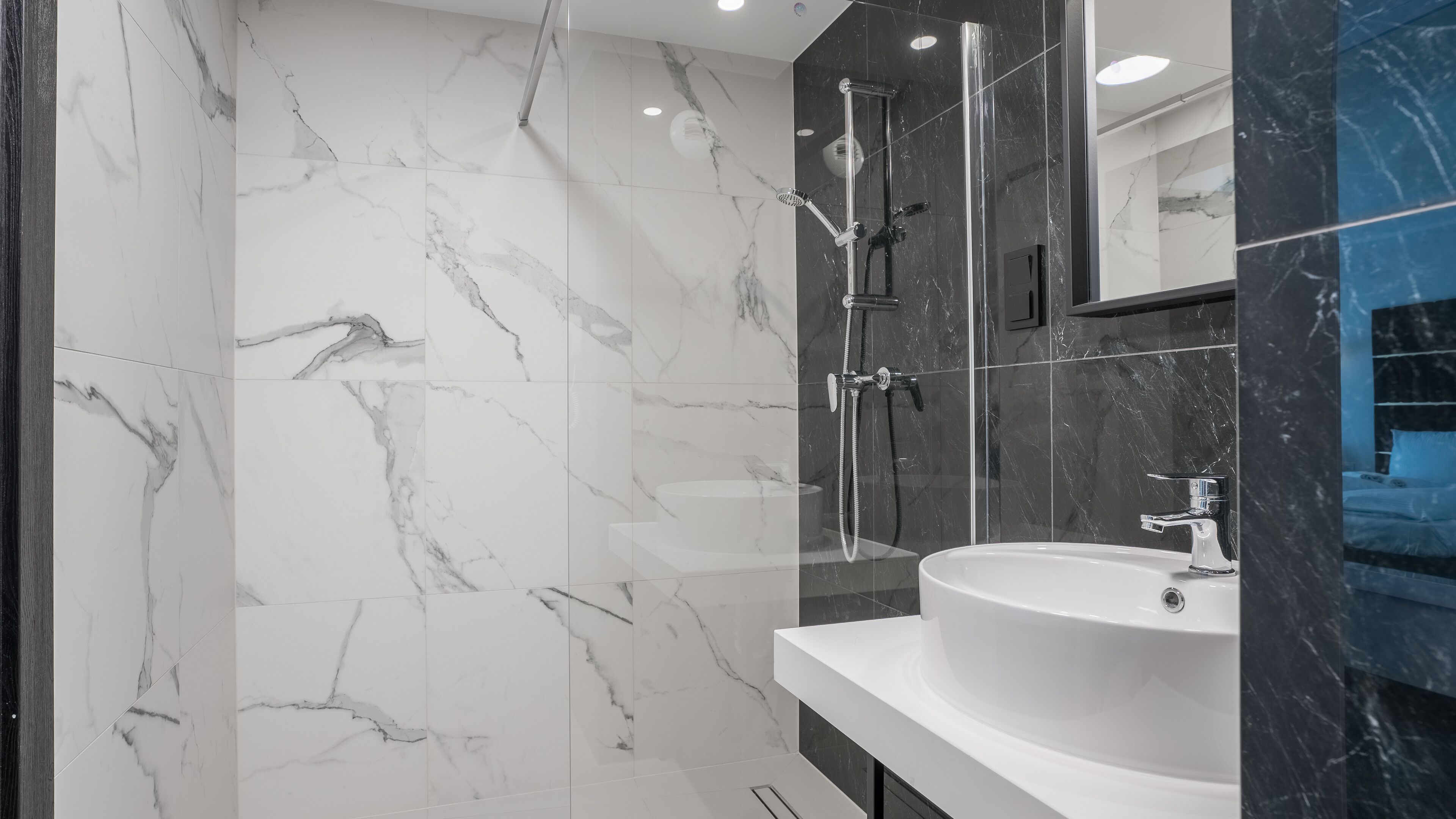 Une salle de bain moderne avec une douche à parois de verre, un lavabo blanc et des murs en marbre.