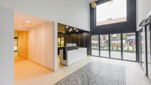 A modern reception area with a reception desk, a patterned rug, and a view of the outside through large windows. - Apartamenty Sun & Snow Solny Resort (Kolobrzeg)