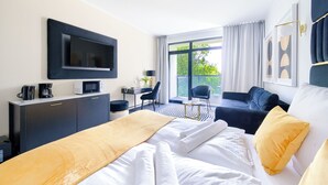 A hotel room with a bed, a desk with a computer, a chair, a sofa, and a TV mounted on the wall. - Apartamenty Sun & Snow Solny Resort (Kolobrzeg)