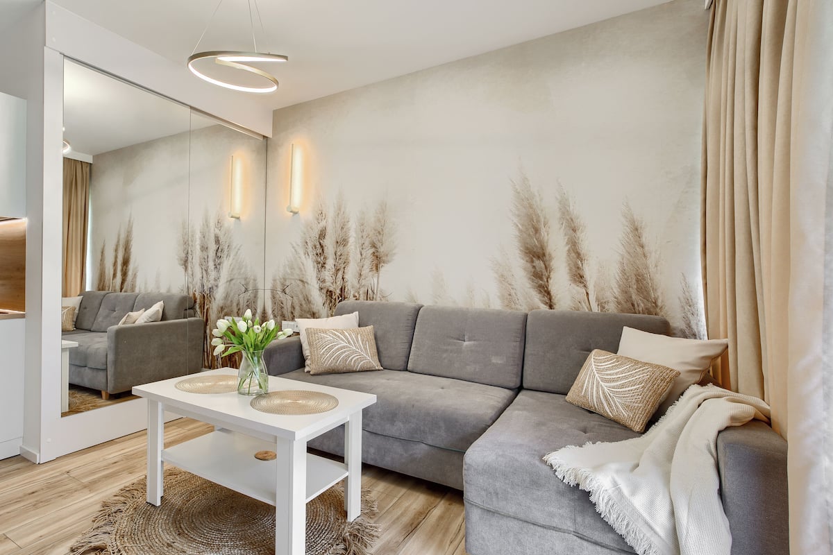 A modern living room with a grey sofa, a white coffee table, and a kitchen area with a kettle.