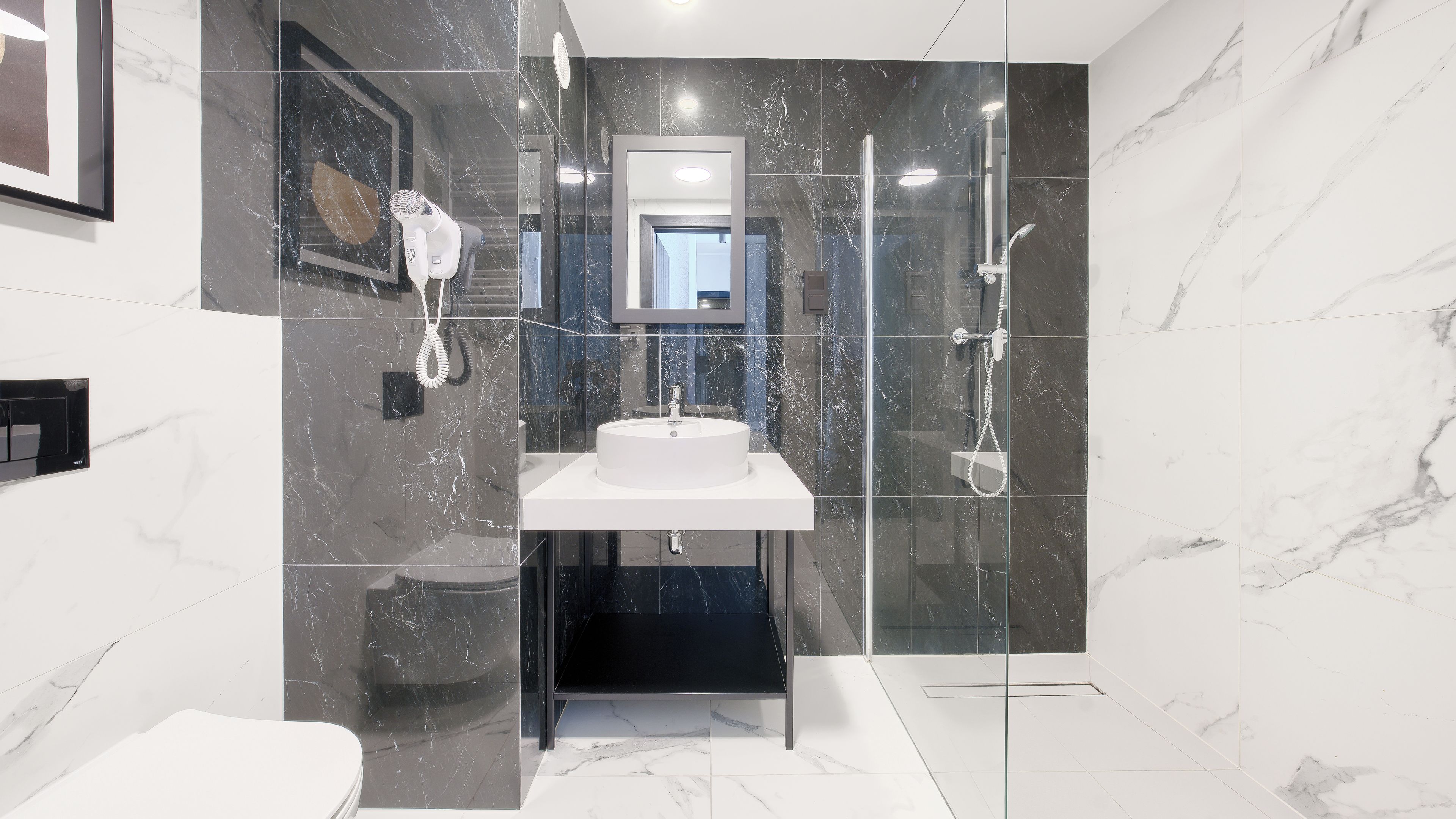 A modern bathroom with a marble sink, a glass-enclosed shower, and a framed picture on the wall.