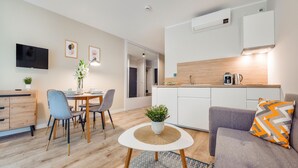 A modern living room with a dining area, a kitchen, and a TV mounted on the wall. - Apartamenty Sun & Snow Solny Resort (Kolobrzeg)
